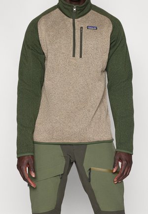 Mężczyzna ubrany w polar na zamek z zielonymi rękawami i beżowym tułowiem, zestawiony z oliwkowozielonymi spodniami bojówkami z wieloma kieszeniami.