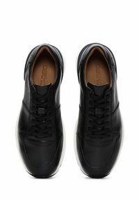 Zapatillas de cuero negro con superficie texturizada, cordones tradicionales y suela de goma blanca. El interior cuenta con una plantilla marrón con detalle de logo.