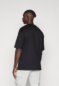 T-shirt nera in cotone con maniche corte e scollatura rotonda, mostrata da dietro, abbinata a pantaloni cargo grigio chiaro.