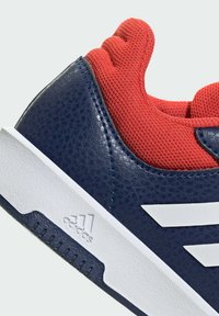 Blauwe en rode sportschoen met een gestructureerde leren bovenkant, gewatteerde schacht, witte tussenzool en drie witte strepen logo aan de zijkant.