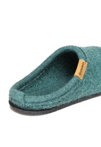Green felt slipper with a soft texture, low back, and brown label. The outer sole is black, and the inner lining appears plush and cozy.