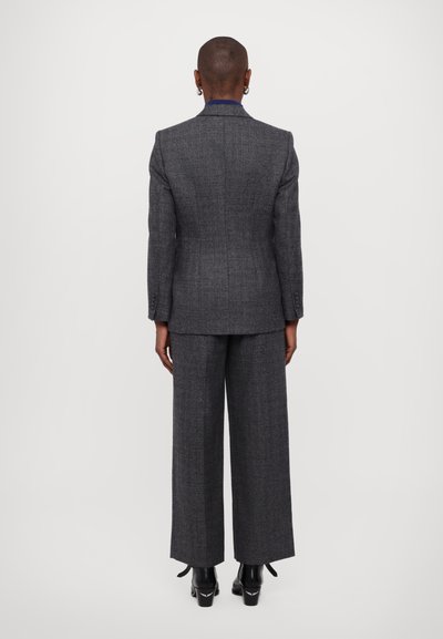 Completo in misto lana grigio con giacca su misura e pantaloni a gamba larga. Il tessuto presenta un leggero motivo a righe. Stivaletti neri con tacco completano il look.