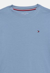 Ανοιχτό μπλε βαμβακερό μπλουζάκι με στρογγυλή λαιμόκοψη, κοντά μανίκια και μικρό κεντημένο λογότυπο σε κόκκινο, λευκό και μπλε στο αριστερό στήθος.