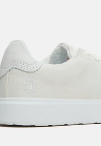 Weiße Leinensneaker mit einem weißen Lederdetail an der Ferse, ausgestattet mit einem dezenten geprägten Logo, tonalem Nähen und einer strukturierten weißen Gummisohle.