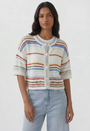 Frau trägt eine kurzärmelige, geknöpfte Strickjacke mit mehrfarbigen horizontalen Streifen über einem weißen Hemd und hellblauen Jeans.