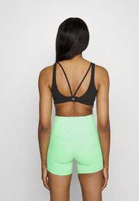 Sutiã desportivo preto com um design nas costas em V e alças finas, combinado com calções de mint verde de cintura alta com uma textura suave e sem fechos visíveis.