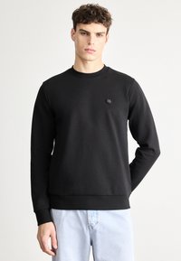 Čierna mikina s dlhými rukávmi, okrúhlym výstrihom a malým logom na hrudi. Vyrobená z hladkej bavlnenej tkaniny, s rebrovaným lemom.