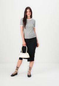 Siva in bela črtasta majica s kratkimi rokavi in gumbi spredaj, črna denim midi krila, črne čevlje z vezalkami in majhna bela torbica.
