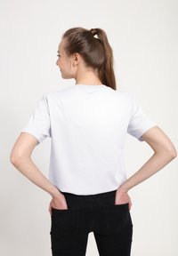 Bílý bavlněný tričko s krátkým rukávem, kulatým výstřihem, volným střihem, nošené s černými džíny; jednoduchý zadní pohled, žádné viditelné logo nebo vzory.