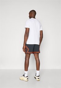 Hvid kortærmet t-shirt, sorte shorts med orange geometriske detaljer, hvide sokker og lyse sneakers, set bagfra.