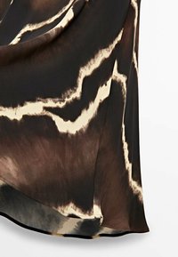 Vêtement en soie marron et crème à la coupe fluide, présentant un motif ondulé et un ourlet courbé, mettant en valeur une texture douce et une sensation de légèreté.