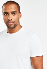 Valkoinen pyöreäkauluksellinen t-paita, joka on valmistettu puuvillasta. Lyhyet hihat, sileä pinta, slim fit -design, minimaalinen ommel yksityiskohtana kauluksessa.