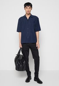 Camisa de manga corta azul marino con rayas verticales, cierre delantero de botones, un bolsillo en el pecho; combinada con pantalones negros y un bolso negro holgado.