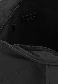 Bolso acolchado negro con cierre de cremallera; forro interior suave; etiqueta de cuero de marca visible en el interior; forma estructurada con bordes sólidos.