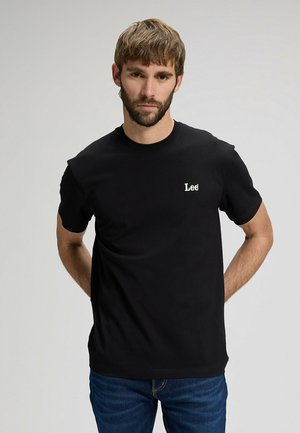 Czarny bawełniany t-shirt z okrągłym dekoltem i krótkimi rękawami, z białym logo „Lee” na lewej piersi. Noszony z niebieskimi dżinsami.