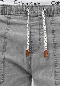 Sive kratke hlače od teksturirane tkanine, elastična waistband s logom i bijelim uzicama s smeškim kožnim naglascima.