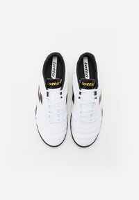 Baskets blanches en matériau synthétique avec une finition texturée, dotées de semelles et d'accents noirs, ainsi que d'un logo doré "lotto" sur la languette.
