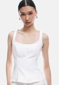 Witte, aansluitende tanktop met een vierkante halslijn en brede banden, met verticale naden voor structuur en een peplumzoom. Gladde textuur.