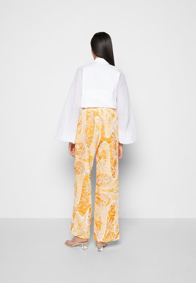 Camisa branca de manga curta com mangas texturizadas, combinada com calças largas amarelas com um padrão tropical. Sandálias de salto transparente.