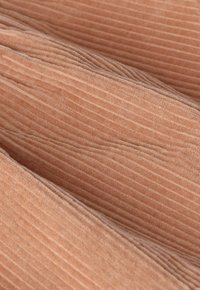 Tissu en velours côtelé de couleur pêche douce avec des côtes verticales visibles et des plis créant un motif texturé et en relief.