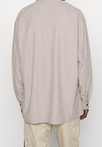 Camicia a quadri beige chiaro con maniche lunghe, polsino con bottoni e orlo arrotondato, realizzata in tessuto strutturato.