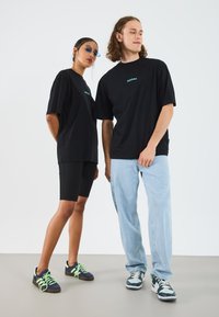 Black oversized t-shirts with embroidered text, paired with black cycling shorts and light blue jeans. Sneakers feature neon green accents.