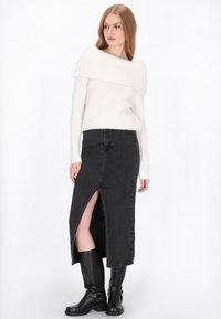 Vállon kívüli, fehér kötött pulóver, amelyet egy fekete farmer maxi szoknyával párosítottak, amelynek combmagas hasítéka van, és fekete térdig érő csizmával.