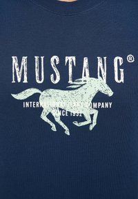 Granatowa bawełniana koszulka z grafiką galopującego konia w jasnej zieleni oraz białym napisem "MUSTANG INTERNATIONAL JEANS COMPANY SINCE 1952."