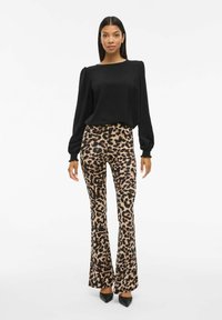 Zwarte langemouwen top met pofschouders, gecombineerd met beige flared pants met een zwart luipaardprintpatroon en puntige zwarte hakken.