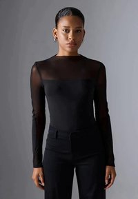 Black long-sleeve top featuring a sheer neckline and sleeves, paired with high-waisted black trousers. Textured fabric with smooth finish.