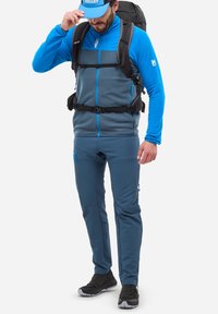 Veste zippée en polaire bleue sur un haut gris, associée à un pantalon bleu. Comprend un sac à dos noir avec des bretelles et des chaussures noires.