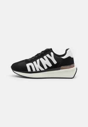Sort-hvid DKNY sneaker med tyk hvid sål, metalaccent på hælen og stort hvidt logotekst på siden.