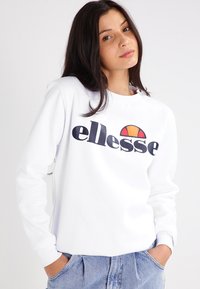 Sudadera blanca de manga larga, con un destacado logo negro "ellesse" y un gráfico de medio sol colorido. Corte casual, textura suave.