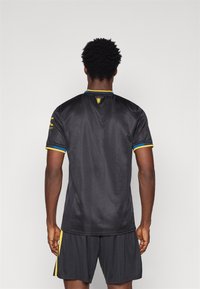 Μαύρη αθλητική μπλούζα με κοντά μανίκια, με κίτρινες και μπλε λεπτομέρειες στον γιακά και στα μανίκια. Υφασμάτινος ιστός με διακριτό �σχέδιο.