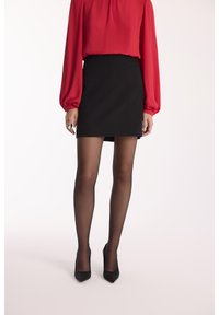 Czarna mini spódniczka o dopasowanym kroju, zestawiona z czerwoną bluzką z długim rękawem. Modelka nosi przezroczyste czarne rajstopy oraz czarne szpilki z ostrym noskiem.