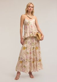 Vestido maxi floral en mezcla de lino, con tirantes finos, volantes en capas, colores pastel con flores rosas y amarillas, y una silueta fluida.