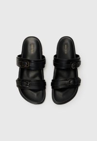Sorte sandaler med to brede stropper, med spenne detaljer, glatt skinnfinish og et flatt, åpent tådesign.