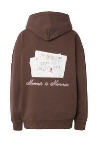 Ruskea huppari, jossa valkoinen revitty paperikuva ja käsinkirjoitettu teksti, jonka takana lukee kursiivilla "Hetkistä muistoiksi".