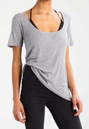 Vrouw draagt een grijs geribd topje met korte mouwen en een ronde hals die een zwarte kanten bralette onthult, gecombineerd met een zwarte broek.