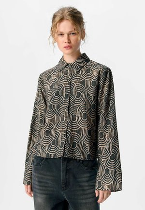Afskåret, knap-op bluse med et svajende mønster i sort og beige, med lange ærmer og en klassisk krave lavet af tekstureret stof.