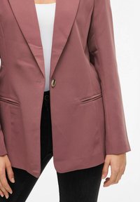Ružičasti sako sa strukturiranim dizajnom, jednim dugmetom i oštrim reverima. Ima bočne džepove i glatku teksturu tkanine.