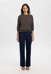 Maglia grigia a maniche lunghe con spalle arricciate, abbinata a jeans a gamba dritta blu scuro e tacchi beige a punta. Tessuto morbido, vestibilità rilassata.