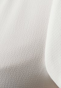 Tessuto strutturato in beige chiaro e bianco, con una superficie morbida e pelosa. Presenta un motivo fine e in rilievo su tutto il materiale.