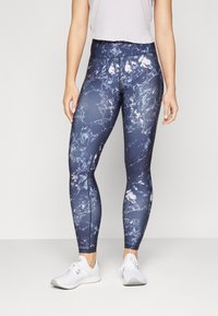 Marina blå leggings med ett marmorerat vitt mönster, hög midja och elastiskt material, kombinerat med vita träningsskor.