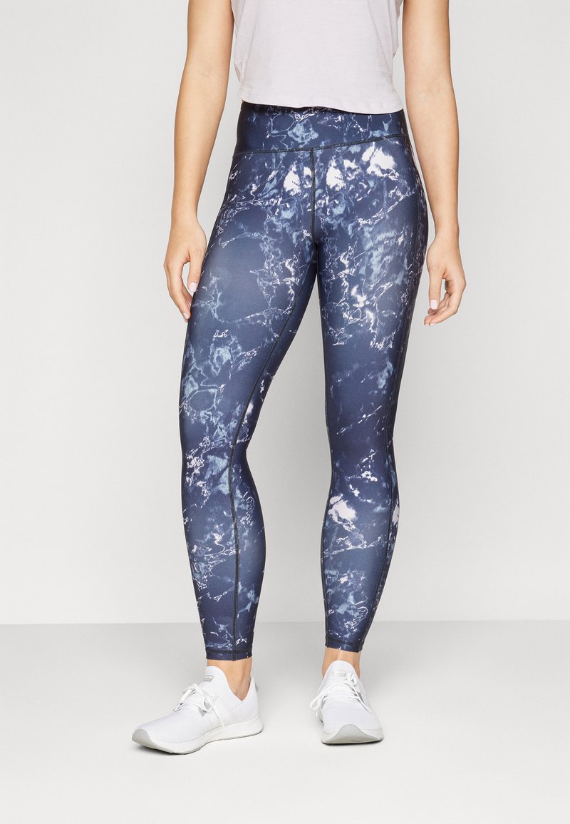 Marina blå leggings med ett marmorerat vitt mönster, hög midja och elastiskt material, kombinerat med vita träningsskor.