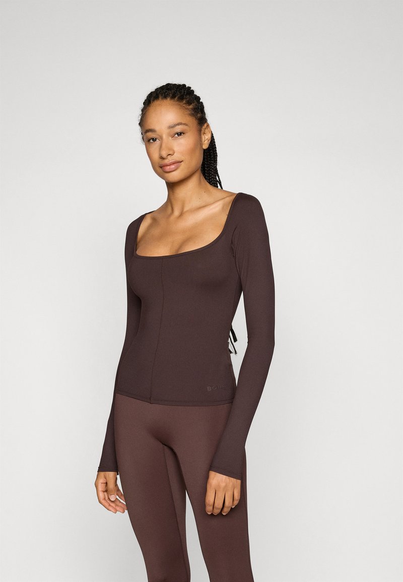 Långärmad, figurnära topp i mörkbrunt ribbat tyg med fyrkantig halsringning och subtila sömdetaljer, matchad med leggings.