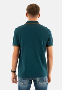 Donkergroene polo met geribbelde kraag en mouwaccenten in goud, gemaakt van een gladde stof, met een rechte snit en korte mouwen.