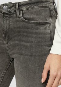 Sive traperice slim kroja, s klasičnom kopčom na dugme, prednjim džepovima i glatkom teksturom. Nema vidljivih uzoraka ili detalja od hardvera.