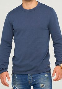 Navyblauer Langarm-Pullover mit Rundhalsausschnitt aus geripptem Stoff. Mit geradem Saum und leicht strukturierter Oberfläche. Kombiniert mit zerstörten Jeans.