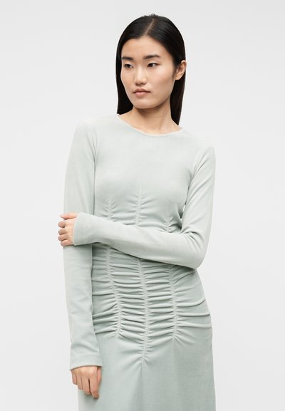 Obleka z dolgimi rokavi iz mehke, svetlo zelene tkanine z naborki na sprednji strani. Gladek tekstura in okrogel izrez na vratu.